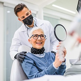 Woman smiling at reflection in handheld mirror with dentist