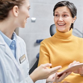 Patient in yellow sweater smiling at dentist holding tablet